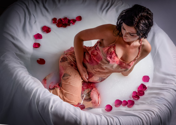 Zartes Milchbad-Shooting für Schwangere Schwangere im Milchbad mit Blumen im Wasser